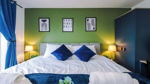 Una habitación de hotel con una cama, dos lámparas de noche, una cortina azul y una obra de arte en la pared.