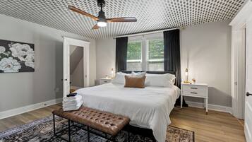 A bedroom with a bed, a bench, a ceiling fan, a nightstand, and a window with curtains.