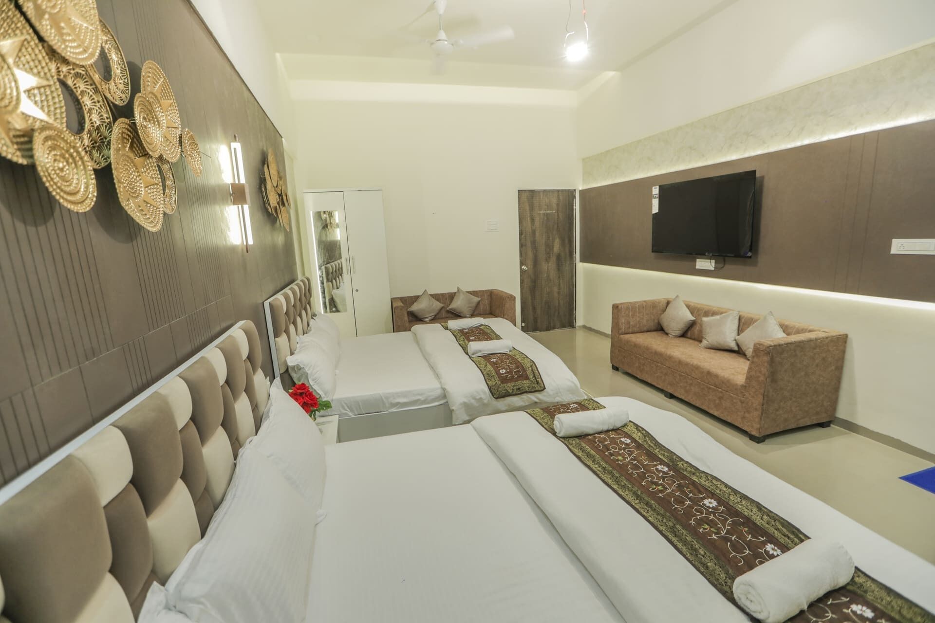 A hotel room with two beds, a sofa, a TV, and a mirror.