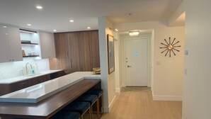 A modern kitchen with a central island, bar stools, wooden cabinets, and a decorative wall piece.