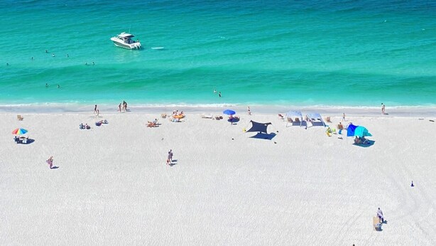 A beach with clear turquoise water, a boat, and people enjoying the sand and sea.