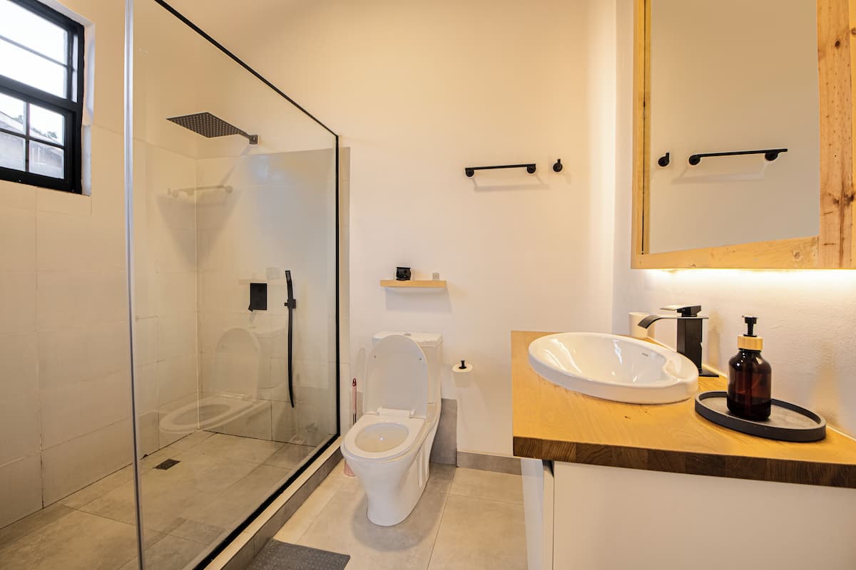 A modern bathroom with a glass-enclosed shower, a white toilet, and a wooden vanity with a sink.