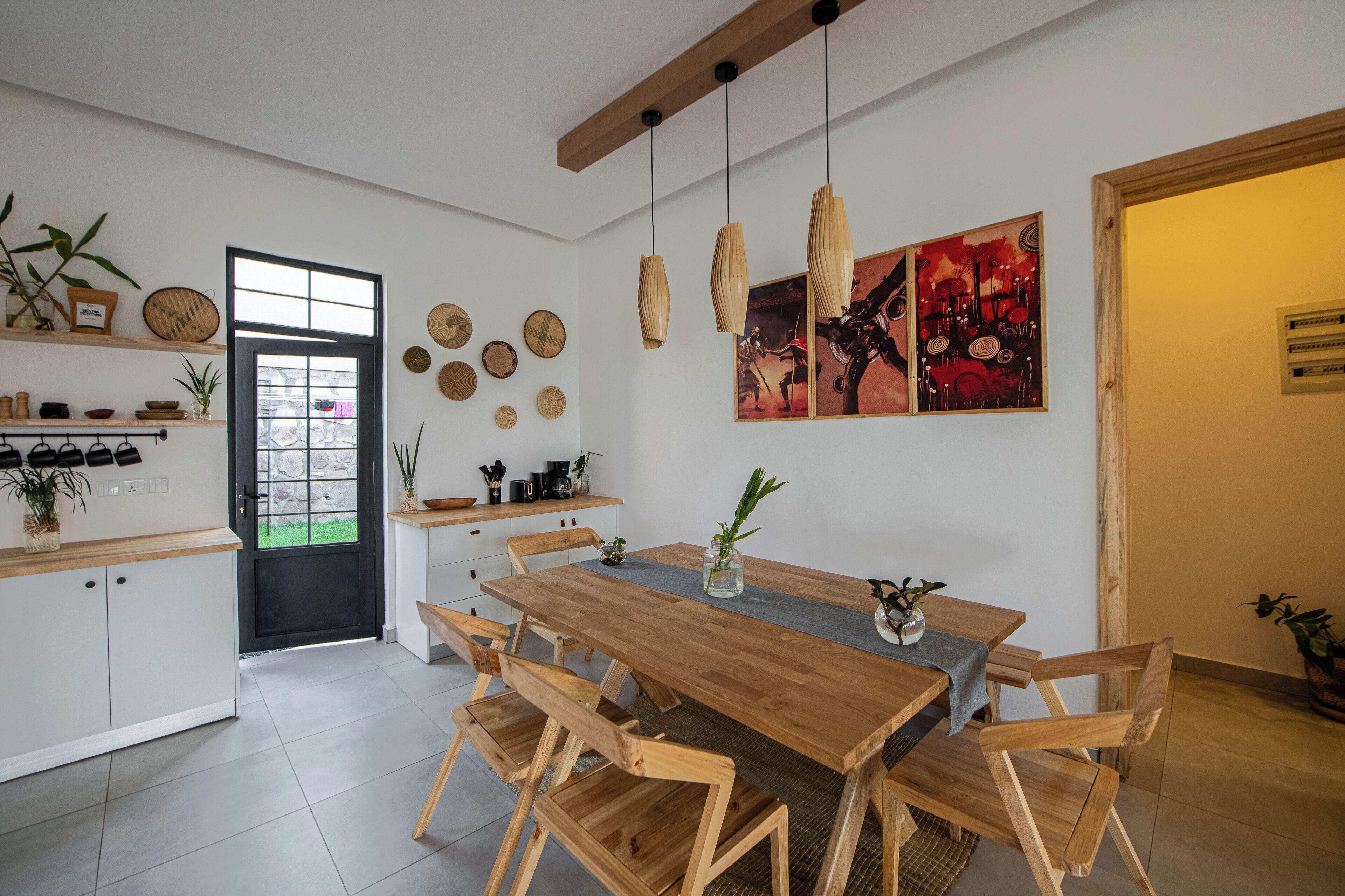 A modern kitchen with a wooden dining table, white cabinets, and a black door.