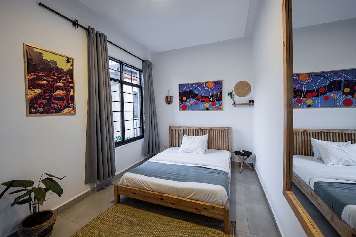 A modern bedroom with two beds, a large window with curtains, and artwork on the walls.