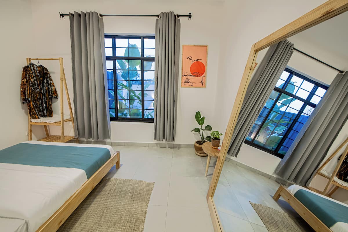 A bedroom with two beds, a large window, a mirror, and a potted plant.