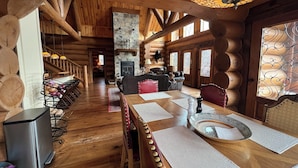 A rustic log cabin interior with a stone fireplace, wooden dining table, and a cozy seating area.