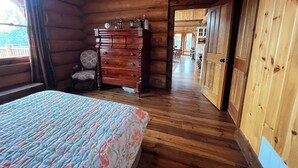 A wooden cabin room with a bed, dresser, and a view of the outside.