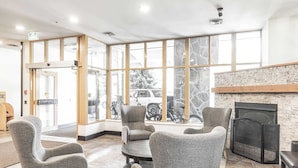 A lobby with grey upholstered chairs, a fireplace, and large windows with a view of parked bicycles.