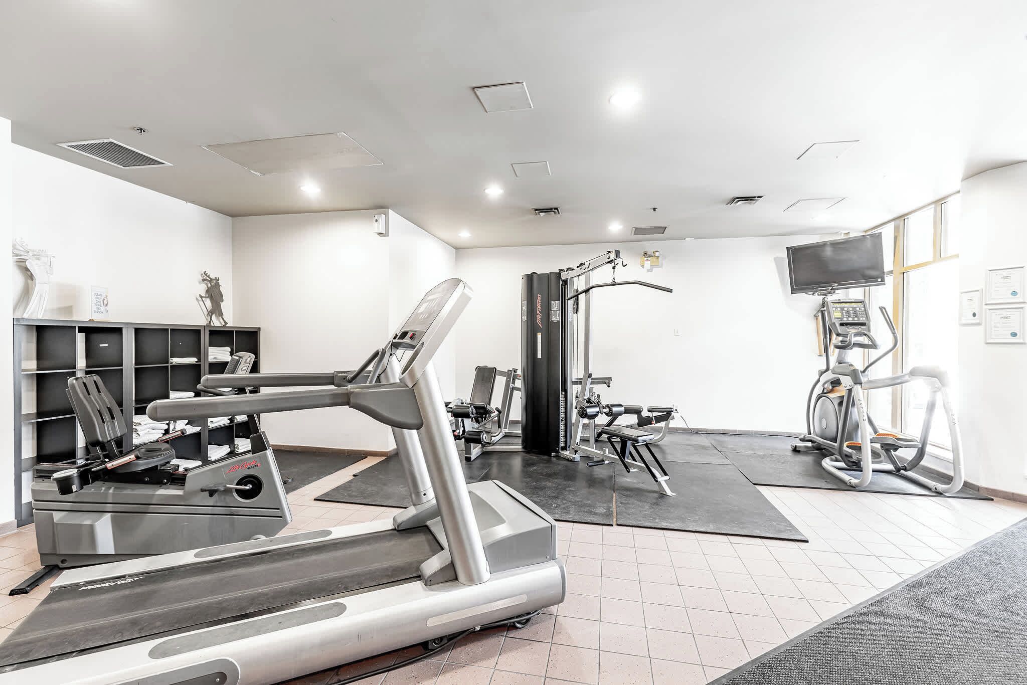 A modern gym with various exercise equipment, including treadmills and weight machines, and a large mirror on the wall.
