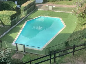 Une piscine rectangulaire dont les bords sont recouverts de carreaux, entourée d’une pelouse bien entretenue et d’une clôture en métal.
