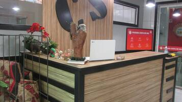 Una recepción con detalles de madera, un gran logotipo en forma de 'S' y una pantalla digital que muestra 'Pousada Costa do Sol'.