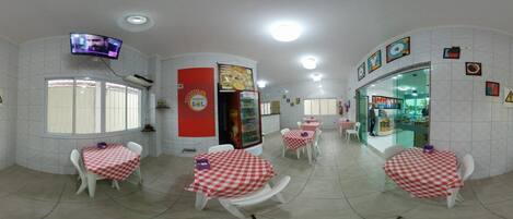 Ein Restaurant mit karierten Tischdecken, weißen Stühlen und einem an der Wand befestigten Fernseher.