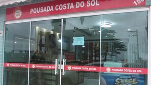 Een etalage met een grote glazen deur, een bord met de tekst 'Pousada Costa do Sol' en het cijfer '158'.