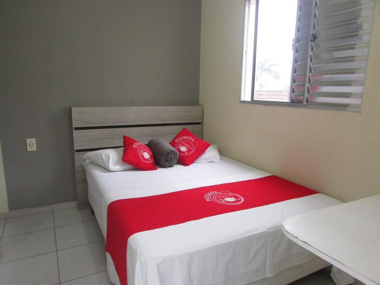 Een net opgemaakt bed met een rood-witte spreideken, twee rode kussens en een opgerolde deken.