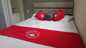 Een net opgemaakt bed met een rode en witte dekbedovertrek, twee rode kussens en een grijze handdoek.