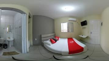 A compact bedroom with a curved bed, a small bedside table, a window with blinds, and a TV mounted on the wall.