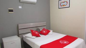 Habitación de hotel con cama, mesita de noche pequeña, aire acondicionado y un cuadro enmarcado en la pared.