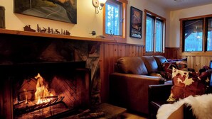A cozy living room with a fireplace, wooden walls, and a couch with a blanket. - Rancho Relaxo, large fully fenced pet friendly lot. Centrally located (Big Bear)
