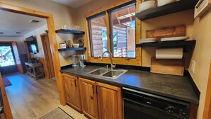 A modern kitchen with wooden cabinets, a dishwasher, a sink, and a window overlooking a wooden deck. - Rancho Relaxo, large fully fenced pet friendly lot. Centrally located (Big Bear)