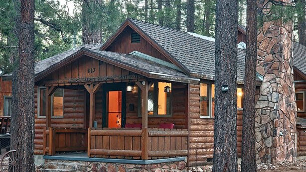 A rustic log cabin with a stone foundation, a porch with seating, and a visible number 812 on the front. - Rancho Relaxo, large fully fenced pet friendly lot. Centrally located (Big Bear)
