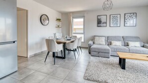 A modern living room with a grey sofa, a wooden coffee table, and a dining area with a table and chairs. - The Cocoon - Appt avec terrasse, 20mn de Toulouse (Castelginest)