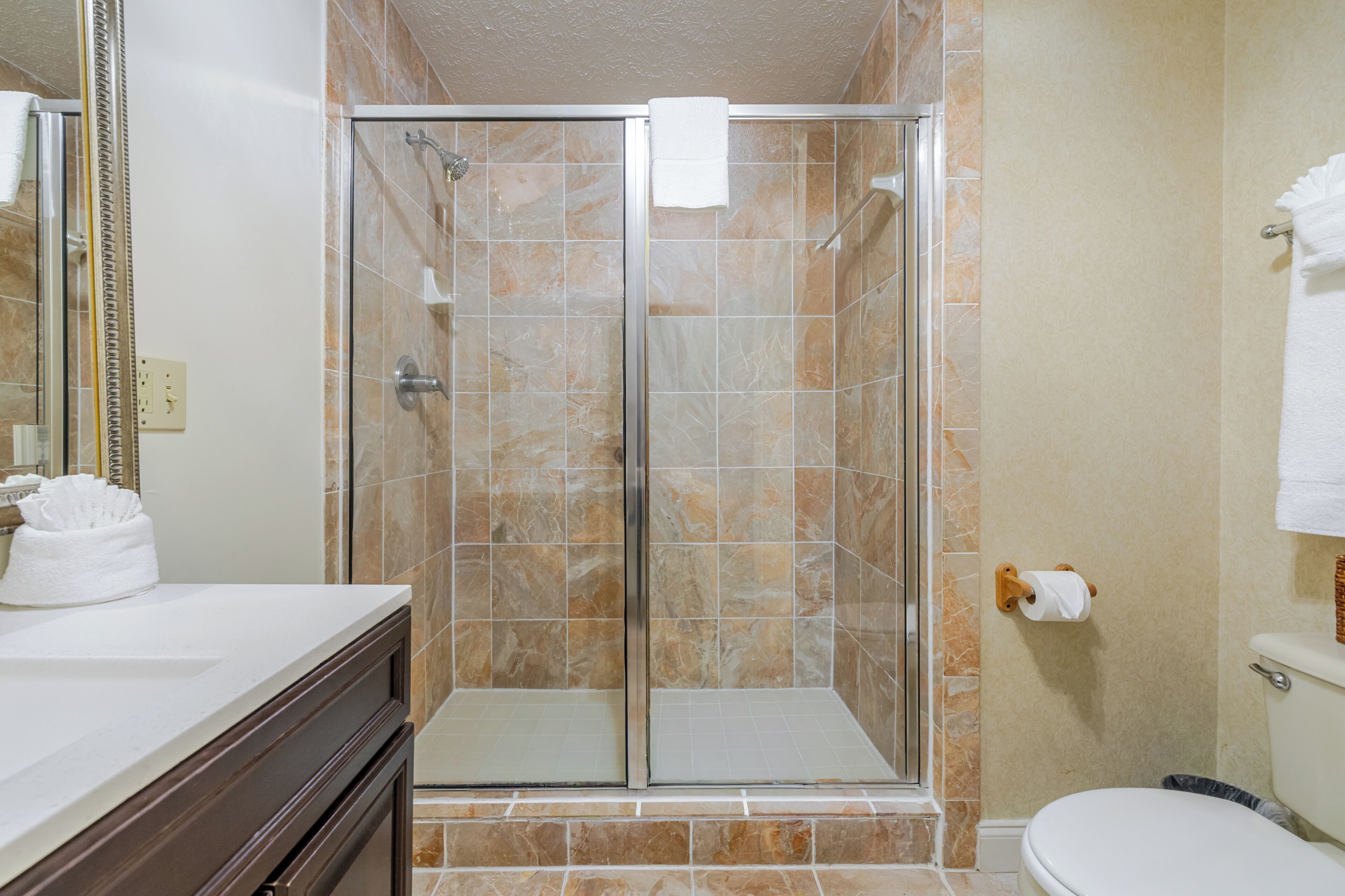 Un baño con ducha envuelta en vidrio, inodoro y lavamanos con espejo.