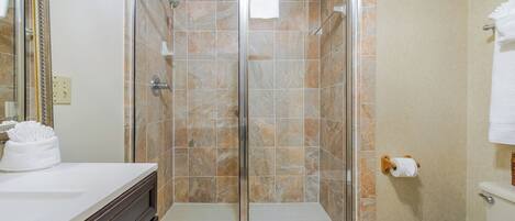 Un baño con ducha envuelta en vidrio, inodoro y lavamanos con espejo.