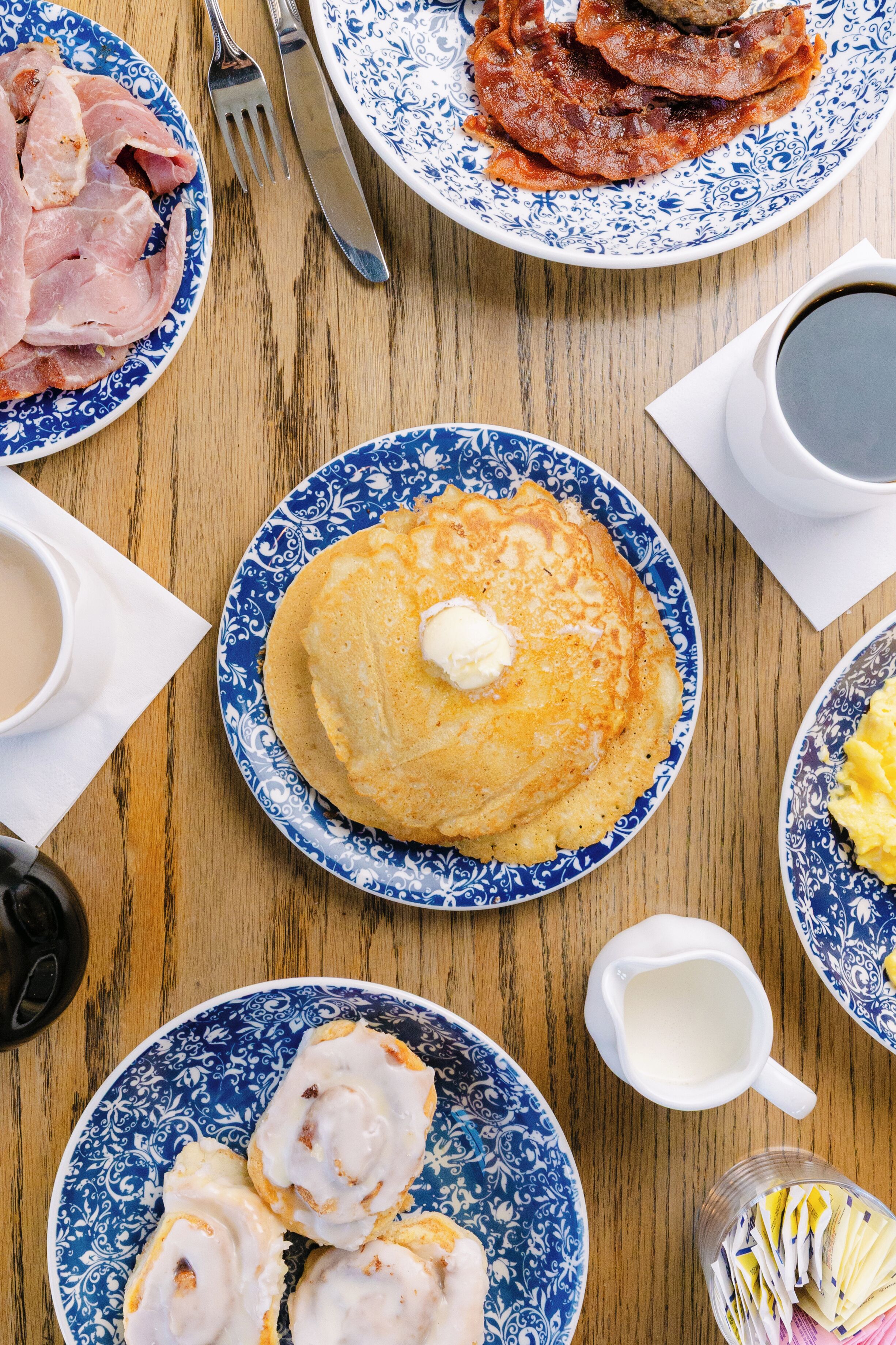 Una mesa de desayuno con platos de comida, una taza de café y una jarra de leche.