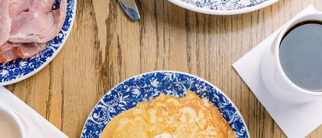 Una mesa de desayuno con platos de comida, una taza de café y una jarra de leche.