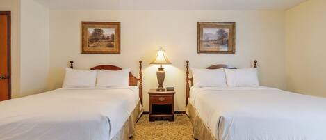 A hotel room with two beds, a nightstand with a lamp, and two framed pictures on the wall.