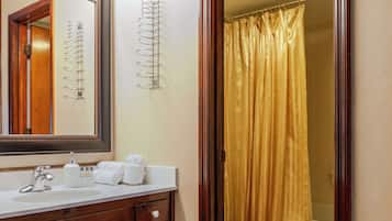 A bathroom with a wooden vanity, a large mirror with lights, a toilet, and a shower curtain.