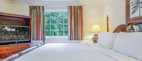 Habitación de hotel con una cama grande, un televisor sobre un mueble de madera, una ventana con cortinas a rayas y una obra de arte floral enmarcada en la pared.