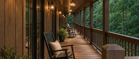 A wooden covered porch with rocking chairs, potted plants, and wall-mounted lanterns.