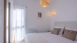 Een slaapkamer met een bed, witte gordijnen, een hanglamp en een klein lijstwerk met een afbeelding aan de muur.