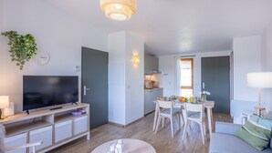 Een moderne woonkamer met een flatscreen televisie, een eethoek met een tafel en stoelen, en een keuken op de achtergrond.