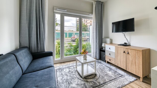 Un salon moderne avec un canapé gris, une table basse blanche, un meuble en bois et un téléviseur fixé au mur.