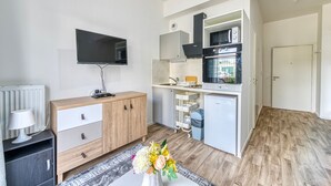 Une cuisine moderne équipée d’un four encastré, d’un four à micro-ondes et d’une cuisinière à gaz. On y trouve un meuble en bois avec des tiroirs et un petit réfrigérateur. Un téléviseur à écran plat est fixé au mur.
