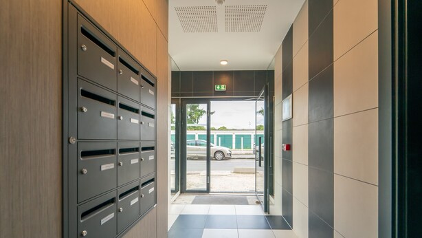 Un hall d’entrée moderne avec un classeur métallique, une porte d’entrée en verre et un sol carrelé.