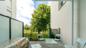 Une petite terrasse avec une table et des chaises, un matelas et une clôture verte.