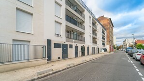 Un immeuble résidentiel à plusieurs étages, doté de balcons, d’une entrée sécurisée et d’un espace de stationnement avec des voitures.