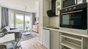 A compact kitchen with a built-in oven and microwave, a small refrigerator, and a dining area with a table and chairs. - Moulin à Vent A14 - Appt pour 4 avec balcon (Bondy)