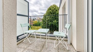 A balcony with two green chairs and a table, a metal railing, and a view of a tree and buildings in the background. - Moulin à Vent A21 - Appt pour 4 (Bondy)