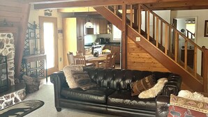 A cozy living room with a leather sofa, a wooden coffee table, and a staircase leading to a kitchen.