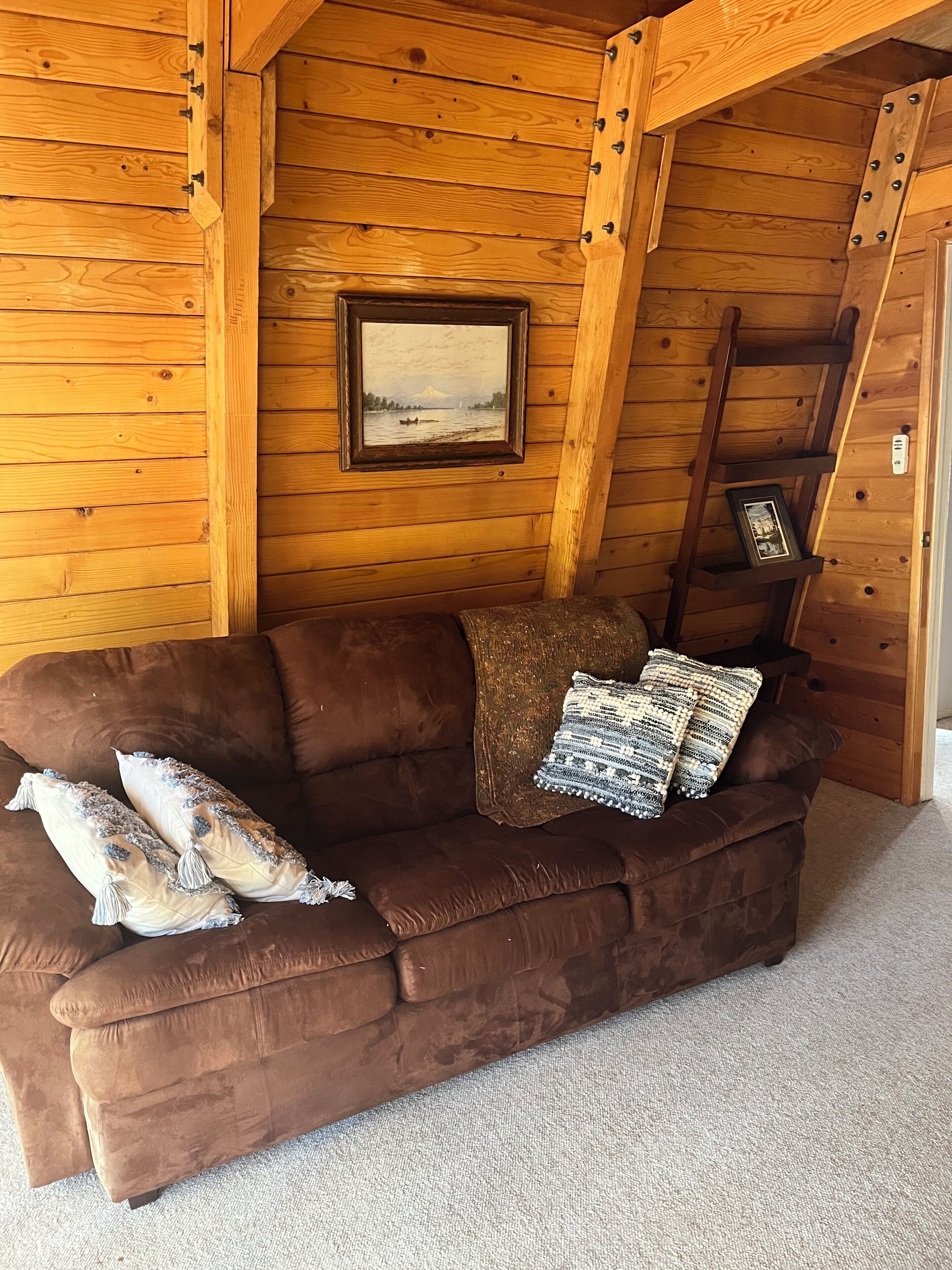 A brown leather couch with decorative pillows and a framed picture on the wall.