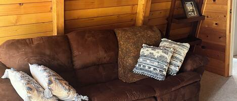 A brown leather couch with decorative pillows and a framed picture on the wall.