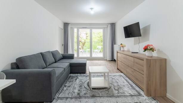 A modern living room with a grey sectional sofa, a white coffee table, a wooden cabinet, and a flat-screen TV mounted on the wall. - Moulin à Vent A22 - Appt pour 4p (Bondy)