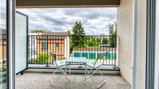 A balcony with two chairs and a table, overlooking a residential area with buildings and a swimming pool. - Moulin à Vent A23 - Appt pour 4p (Bondy)