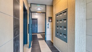 A modern hallway with a checkered floor, a blue door, and a row of mailboxes on the right. - Moulin à Vent A24 - Appt pour 4p (Bondy)