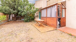 A courtyard with a wooden table and chairs, a covered outdoor seating area, and a large tree.