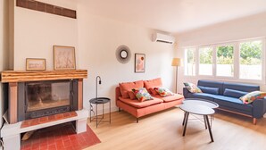 A living room with a fireplace, a sofa, a coffee table, and a window with a view of greenery.